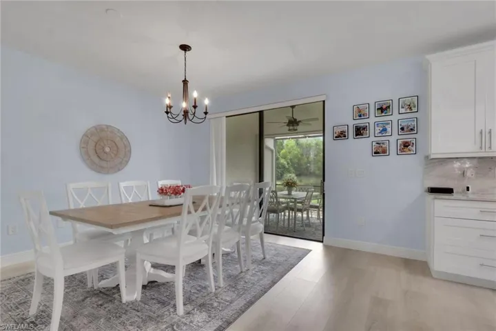 Dining area featuring wood-finish flooring, white shaker-style cabinetry, stone countertops, a multi-light chandelier, and sliding glass doors