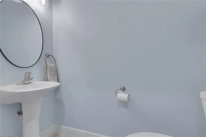 White pedestal sink with a chrome faucet, oval wall-mounted mirror, and wall-mounted metal hardware