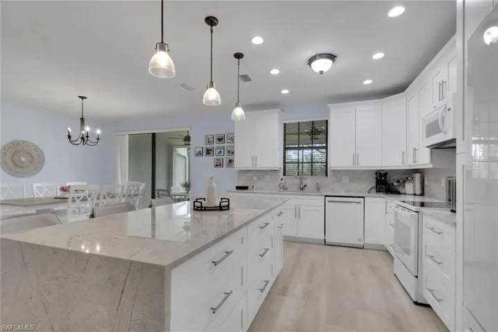 Kitchen featuring a waterfall-edge stone island, white Shaker-style cabinetry, recessed lighting, glass pendant fixtures, and wood-finish flooring