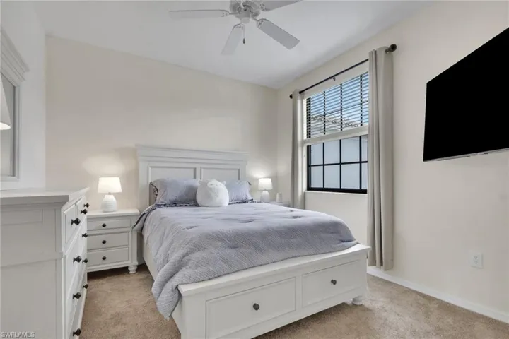 Neutral-toned room featuring wall-to-wall carpeting, a multi-pane window with a black frame, and a white ceiling fan with integrated lighting