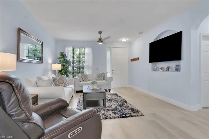 Living area featuring light wood-finish flooring, a recessed arched media niche, and a ceiling fan with integrated lighting