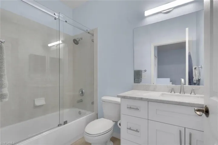 Bathroom featuring a white shaker-style vanity with stone countertop, under-mount sink, glass sliding shower door, and large-format wall tile
