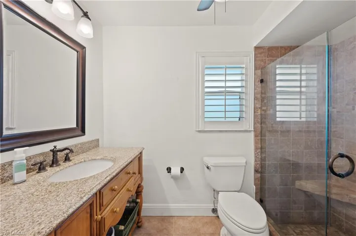 Bathroom featuring tile floors, a shower with shower door, oversized vanity, ceiling fan, and toilet