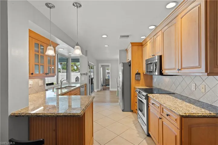 Kitchen featuring light hardwood / wood-style flooring, stainless steel appliances, pendant lighting, dark stone countertops, and backsplash