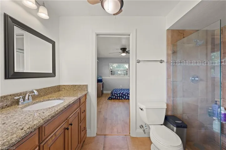 Bathroom featuring tiled shower, tile floors, vanity with extensive cabinet space, ceiling fan, and toilet