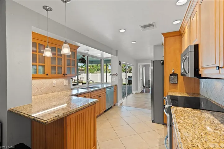 Kitchen with appliances with stainless steel finishes, backsplash, pendant lighting, sink, and light tile floors