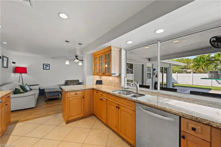 Kitchen with light hardwood / wood-style flooring, kitchen peninsula, stainless steel dishwasher, decorative light fixtures, and sink