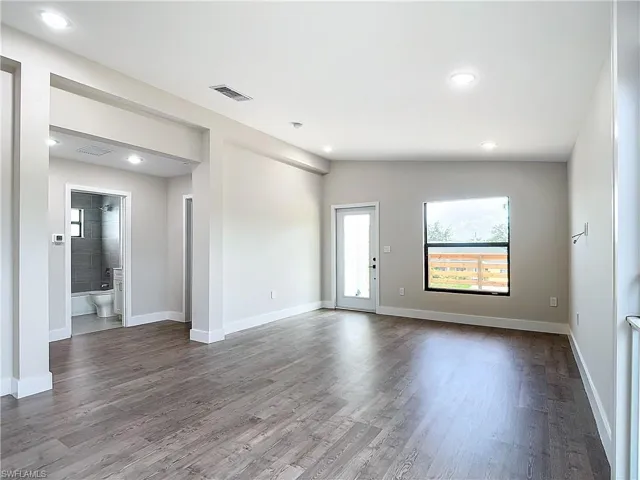 Spare room with baseboards, dark wood-style floors, visible vents, and vaulted ceiling