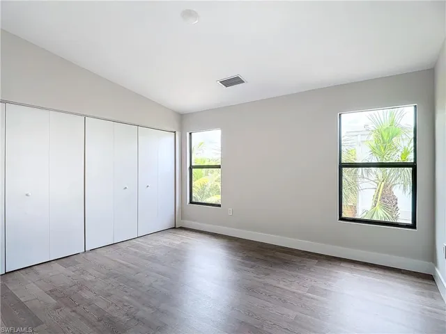 Unfurnished bedroom featuring lofted ceiling, baseboards, visible vents, a closet, and wood finished floors