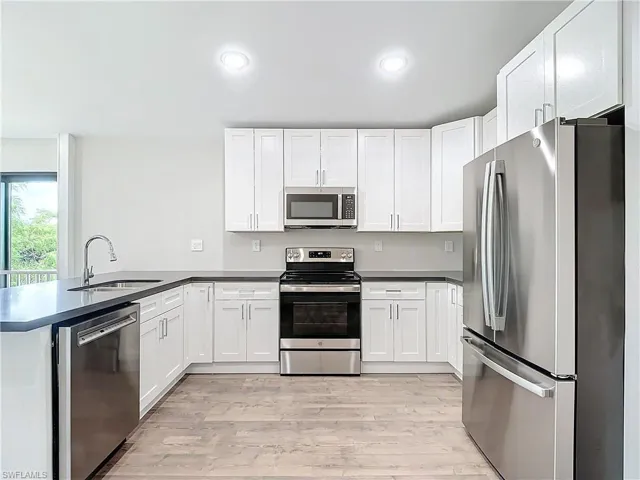 Kitchen with light wood-style flooring, a peninsula, stainless steel appliances, white cabinetry, and a sink