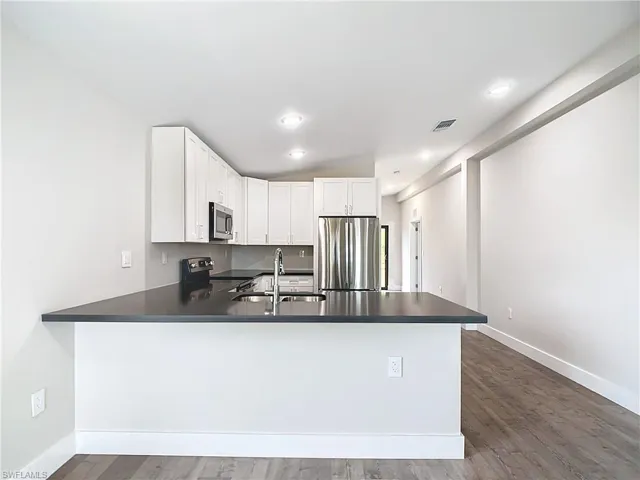 Kitchen featuring white cabinets, visible vents, a peninsula, stainless steel appliances, and a sink