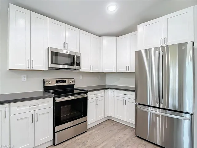 Kitchen featuring white cabinetry, dark countertops, light wood-style flooring, and appliances with stainless steel finishes