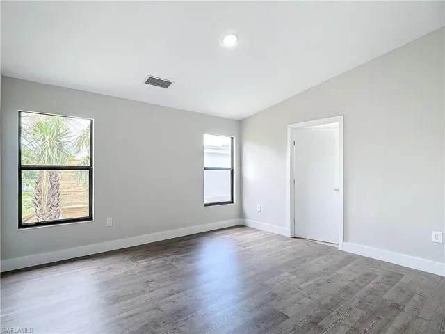 Empty room with lofted ceiling, a wealth of natural light, visible vents, and wood finished floors