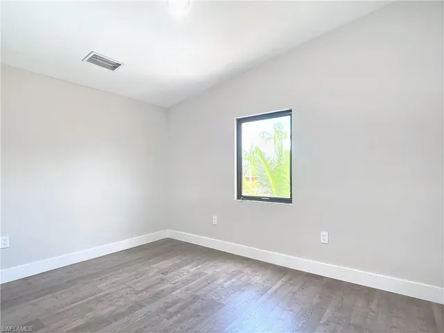 Empty room with dark wood-style floors, visible vents, baseboards, and vaulted ceiling