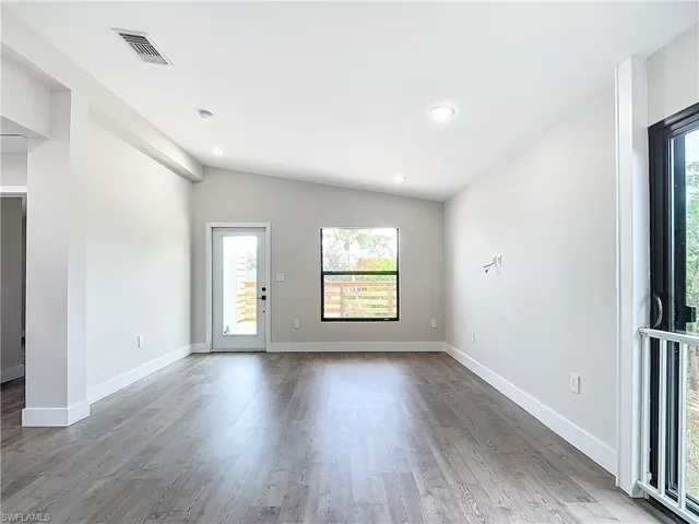 Empty room with baseboards, visible vents, vaulted ceiling, and wood finished floors