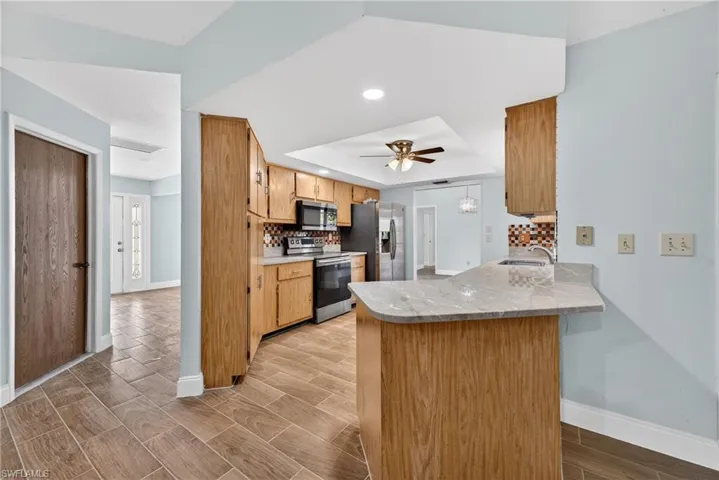 Kitchen with light countertops, wood finish floors, a peninsula, decorative backsplash, and a raised ceiling