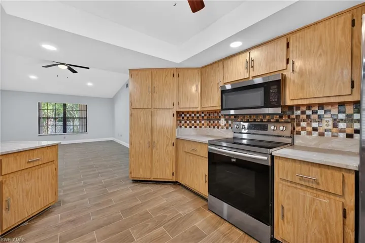 Kitchen featuring a ceiling fan, stainless steel appliances, light countertops, wood finish floors, and lofted ceiling