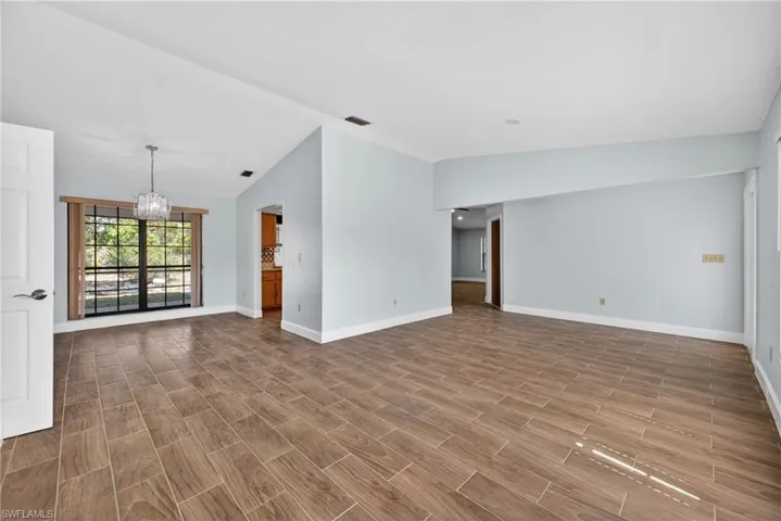 Empty room featuring hanging lights, wood tiled floors, and vaulted ceiling