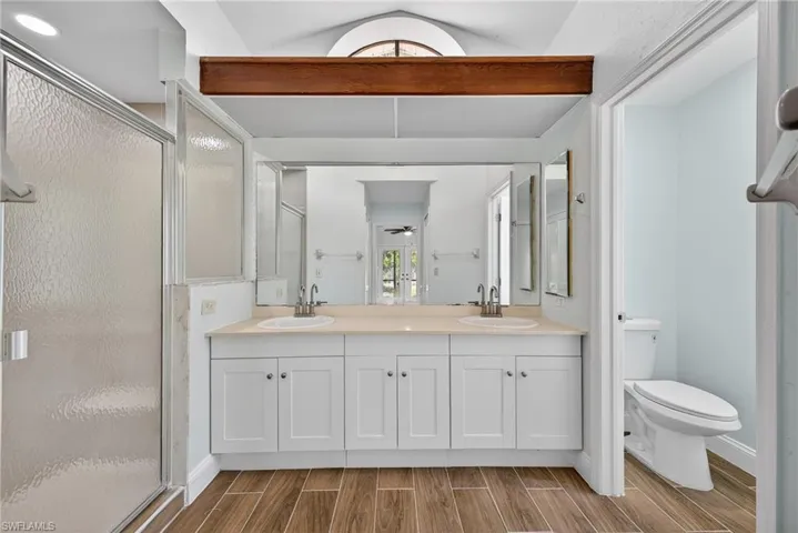Bathroom with wood tiled floors, double vanity, a shower stall, vaulted ceiling, and a ceiling fan