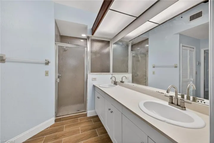 Bathroom featuring double vanity, wood tiled floors, a stall shower, and a closet
