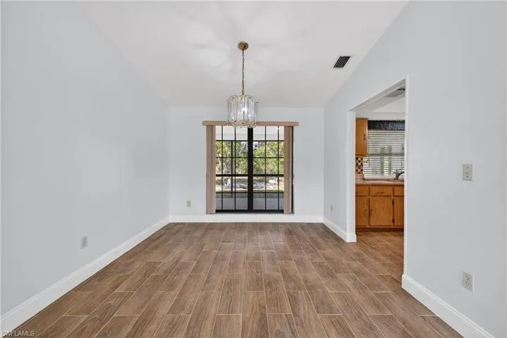Unfurnished dining area with wood finish floors, a chandelier, vaulted ceiling, and plenty of natural light