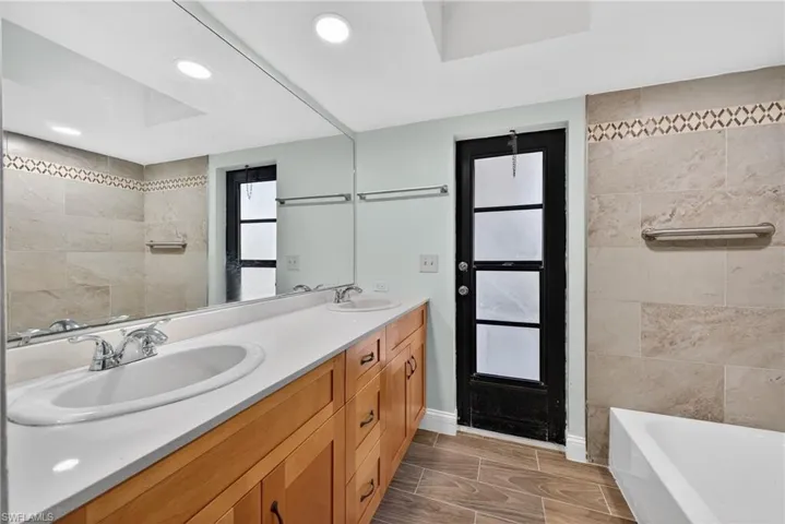 Full bath featuring double vanity, a tile shower, a bath, wood tiled floors, and tile walls