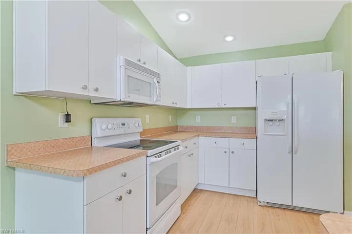 Kitchen featuring vaulted ceiling, white cabinets, white appliances, and light wood-type flooring