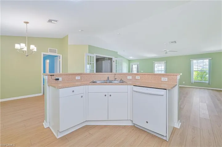 Kitchen with decorative light fixtures, white cabinetry, white dishwasher, sink, and lofted ceiling