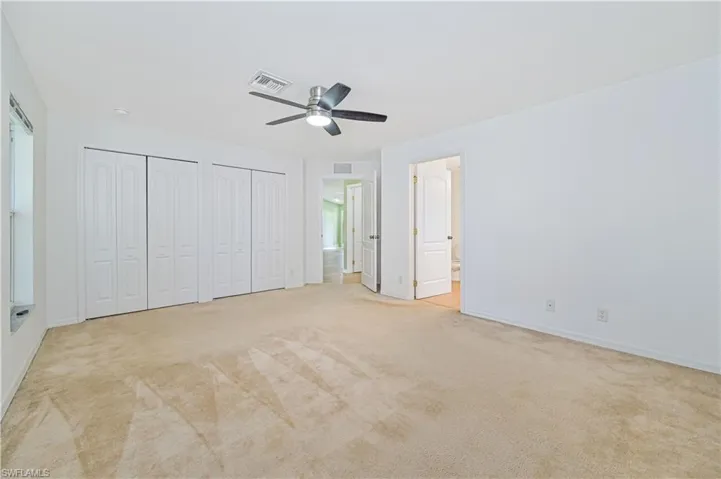Unfurnished bedroom featuring connected bathroom, two closets, ceiling fan, and light colored carpet