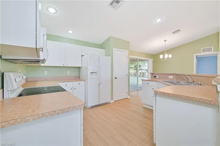 Kitchen featuring hanging light fixtures, stove, white refrigerator with ice dispenser, sink, and lofted ceiling
