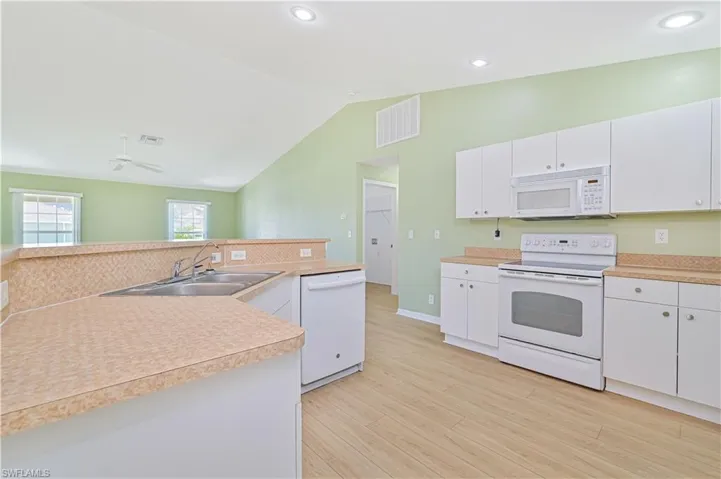 Kitchen featuring vaulted ceiling, ceiling fan, white cabinetry, light wood-type flooring, and white appliances