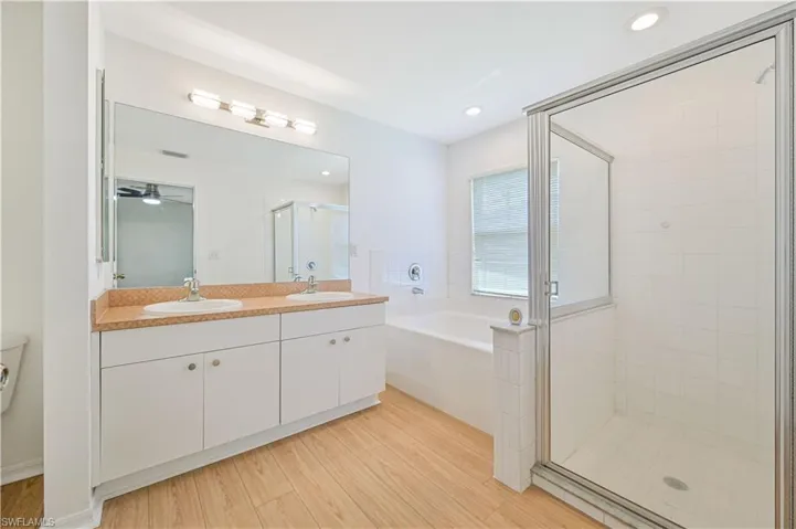 Bathroom featuring ceiling fan, separate shower and tub, double sink vanity, and wood-type flooring