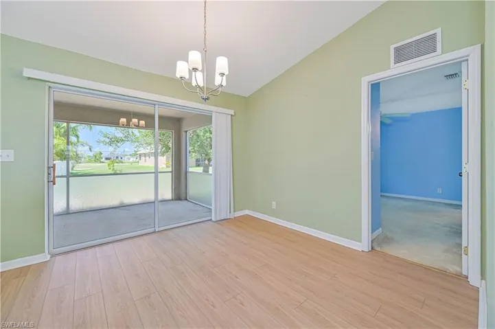 Carpeted spare room featuring a notable chandelier, vaulted ceiling, and a wealth of natural light