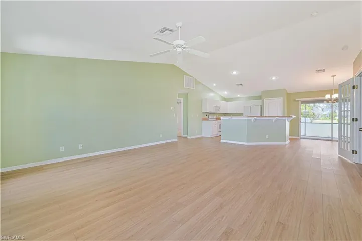 Unfurnished living room featuring light hardwood / wood-style flooring, ceiling fan with notable chandelier, and lofted ceiling