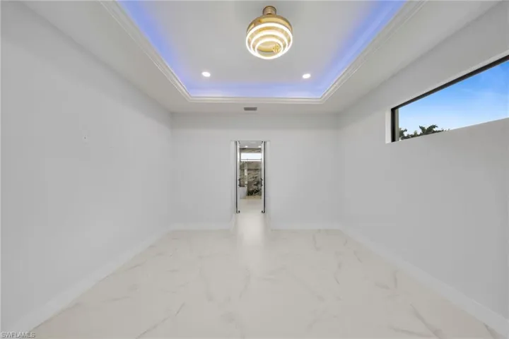 Empty room featuring marble finish flooring, recessed lighting, a raised ceiling, and crown molding