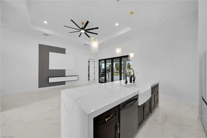 Kitchen with dark cabinets, a tray ceiling, light marble finish flooring, hanging light fixtures, and a kitchen island with sink