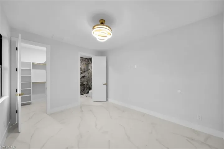 Unfurnished bedroom with light marble finish flooring and a walk in closet