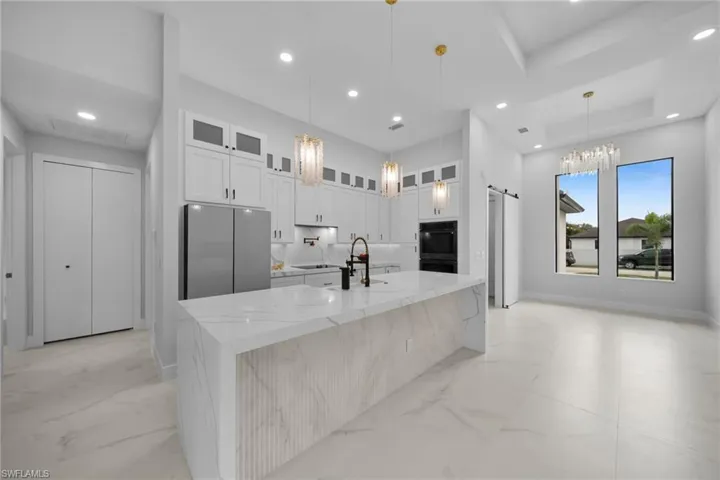Kitchen featuring glass insert cabinets, light stone countertops, an island with sink, white cabinets, and black appliances