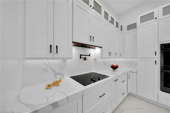 Kitchen with light stone countertops, white cabinets, black appliances, light marble finish floors, and glass insert cabinets