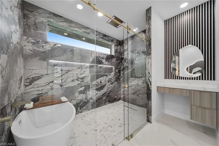 Bathroom featuring marble tiled floors, a marble finish shower, a freestanding bath, recessed lighting, and vanity