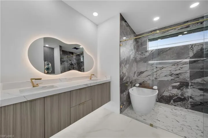 Bathroom with a marble finish shower, double vanity, marble tiled flooring, recessed lighting, and a freestanding tub