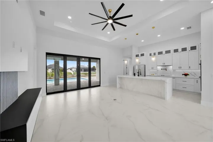 Unfurnished living room with light marble finish floors, recessed lighting, a towering ceiling, a tray ceiling, and a ceiling fan