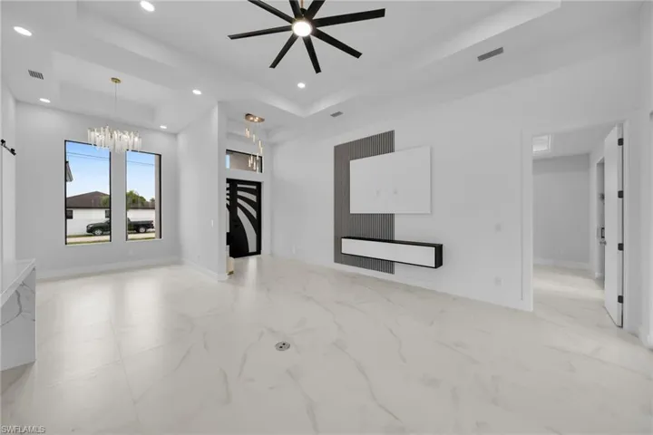 Unfurnished living room with light marble finish flooring, a raised ceiling, a chandelier, recessed lighting, and a ceiling fan