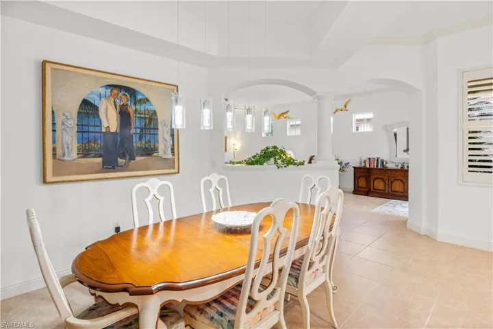 Dining room featuring decorative columns, light tile patterned flooring, arched walkways, and baseboards