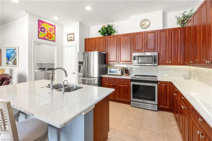 Kitchen featuring appliances with stainless steel finishes, washer and clothes dryer, a sink, light stone countertops, and ornamental molding