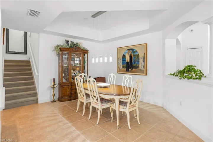 Dining space featuring a tray ceiling, stairway, light tile patterned floors, baseboards, and arched walkways