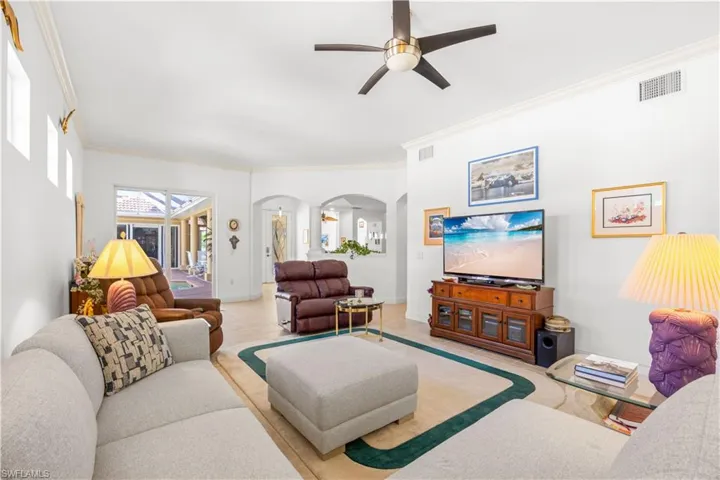 Living room with arched walkways, ornamental molding, a ceiling fan, tile patterned floors, and baseboards
