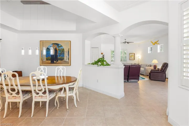 Dining space featuring decorative columns, arched walkways, light tile patterned flooring, crown molding, and baseboards