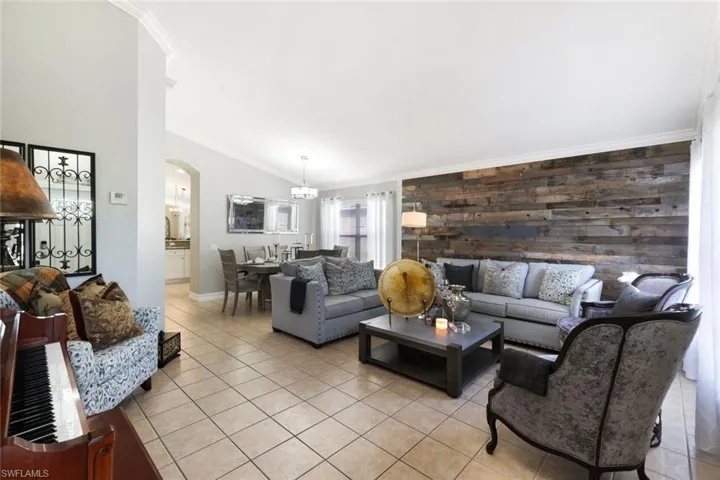 Living room with light tile patterned floors, arched walkways, an accent wall, vaulted ceiling, and crown molding
