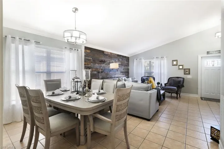Dining area with light tile patterned floors, an accent wall, vaulted ceiling, and crown molding